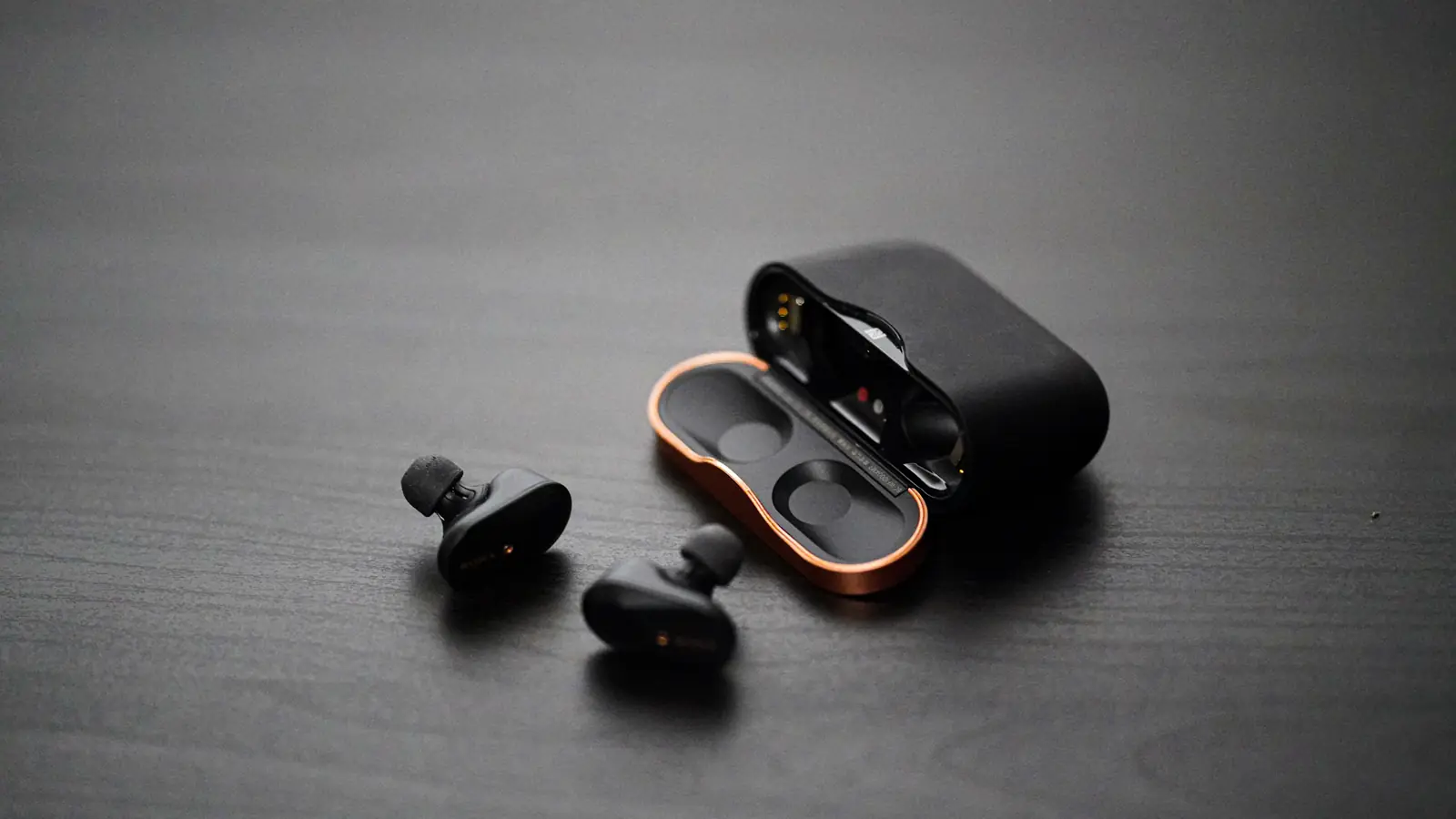 Auricolari true wireless neri con custodia su un piano di lavoro neutro.