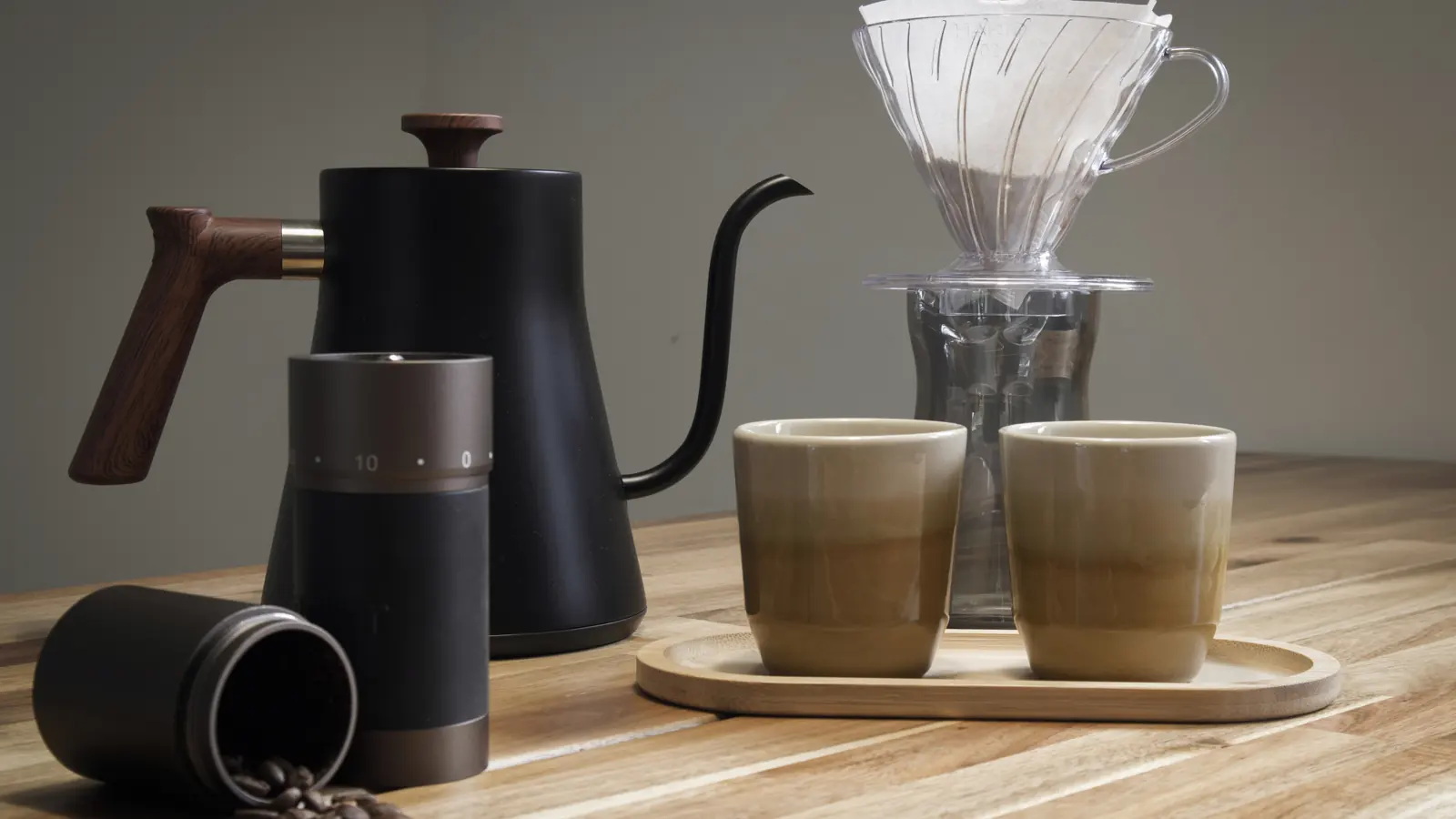 Tavolo con tazze, chicchi e accessori per confrontare diversi modi di preparare il caffè.