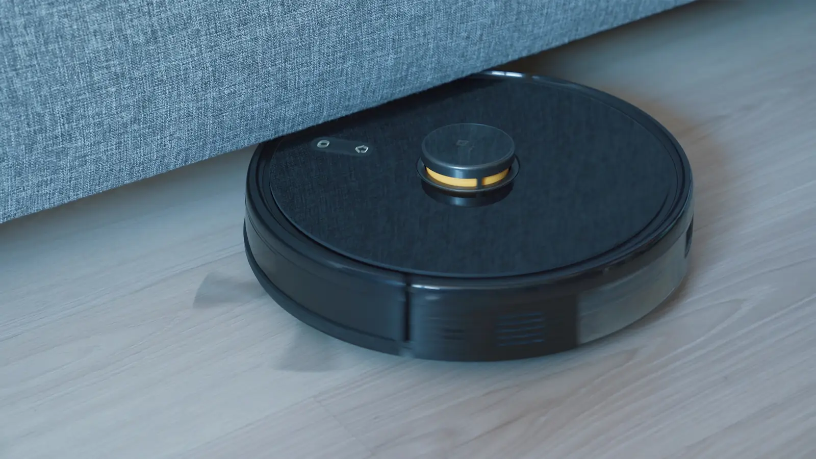 Robot aspirapolvere nero che lavora vicino a un divano in una stanza domestica.
