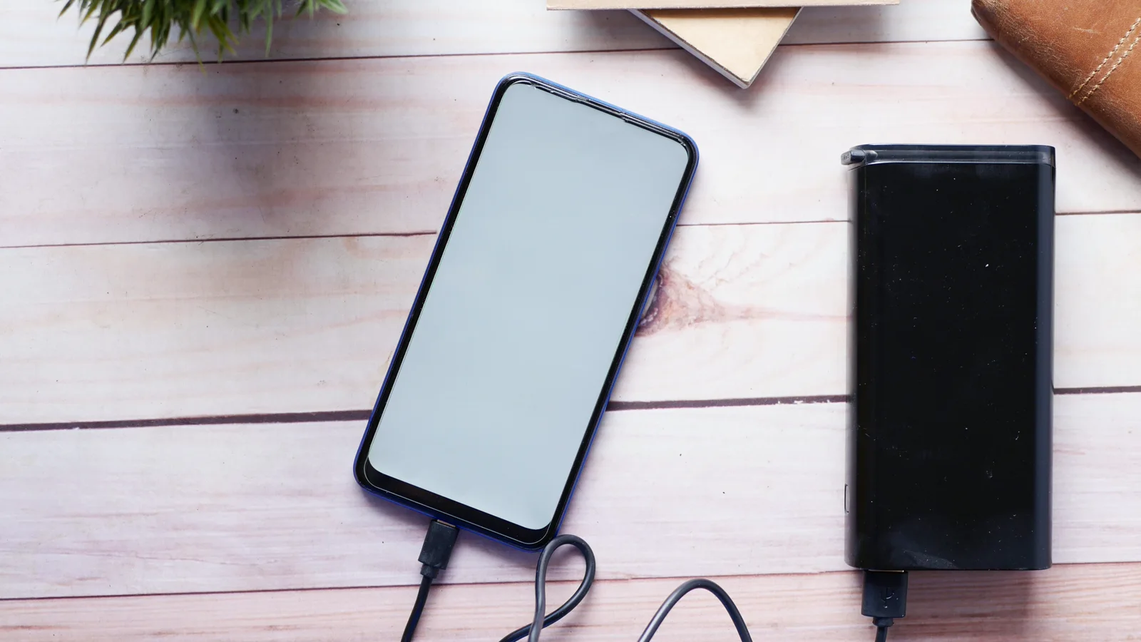Smartphone collegato a un power bank neutro su un tavolo, con il cavo di ricarica visibile.